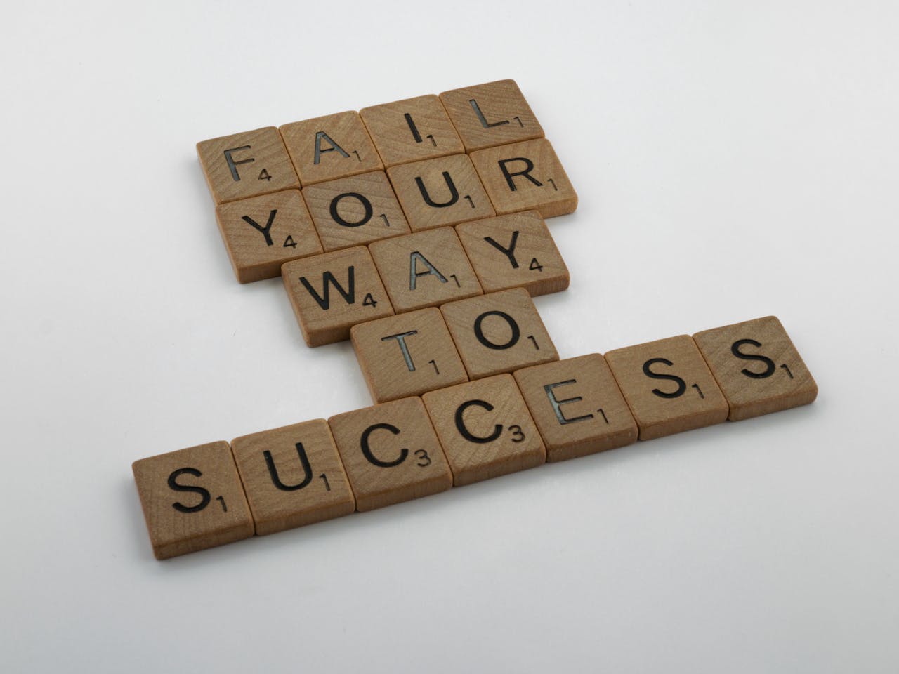 Wooden tiles spell 'Fail Your Way to Success' emphasizing perseverance.
